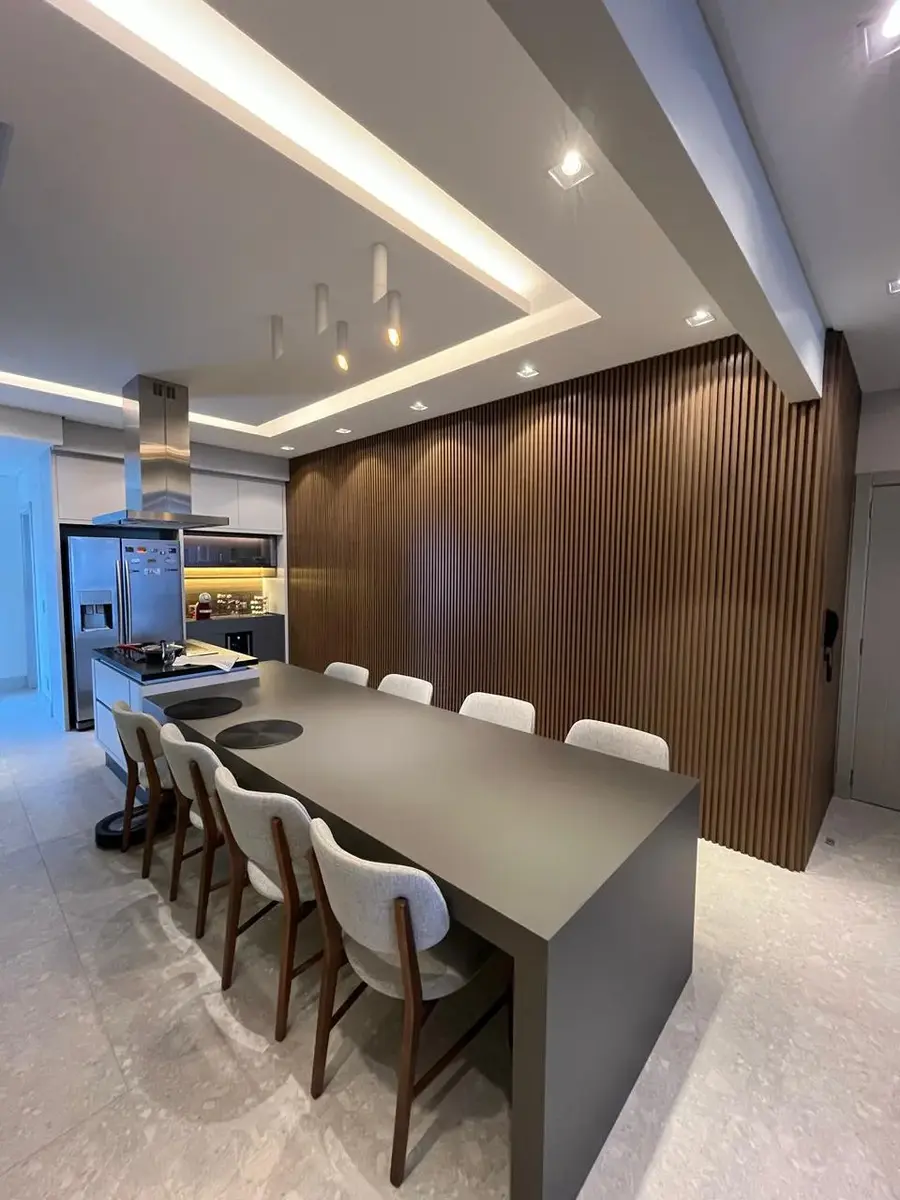 Cozinha planejada com mesa integrada à ilha e parede ripada, projeto da Genova